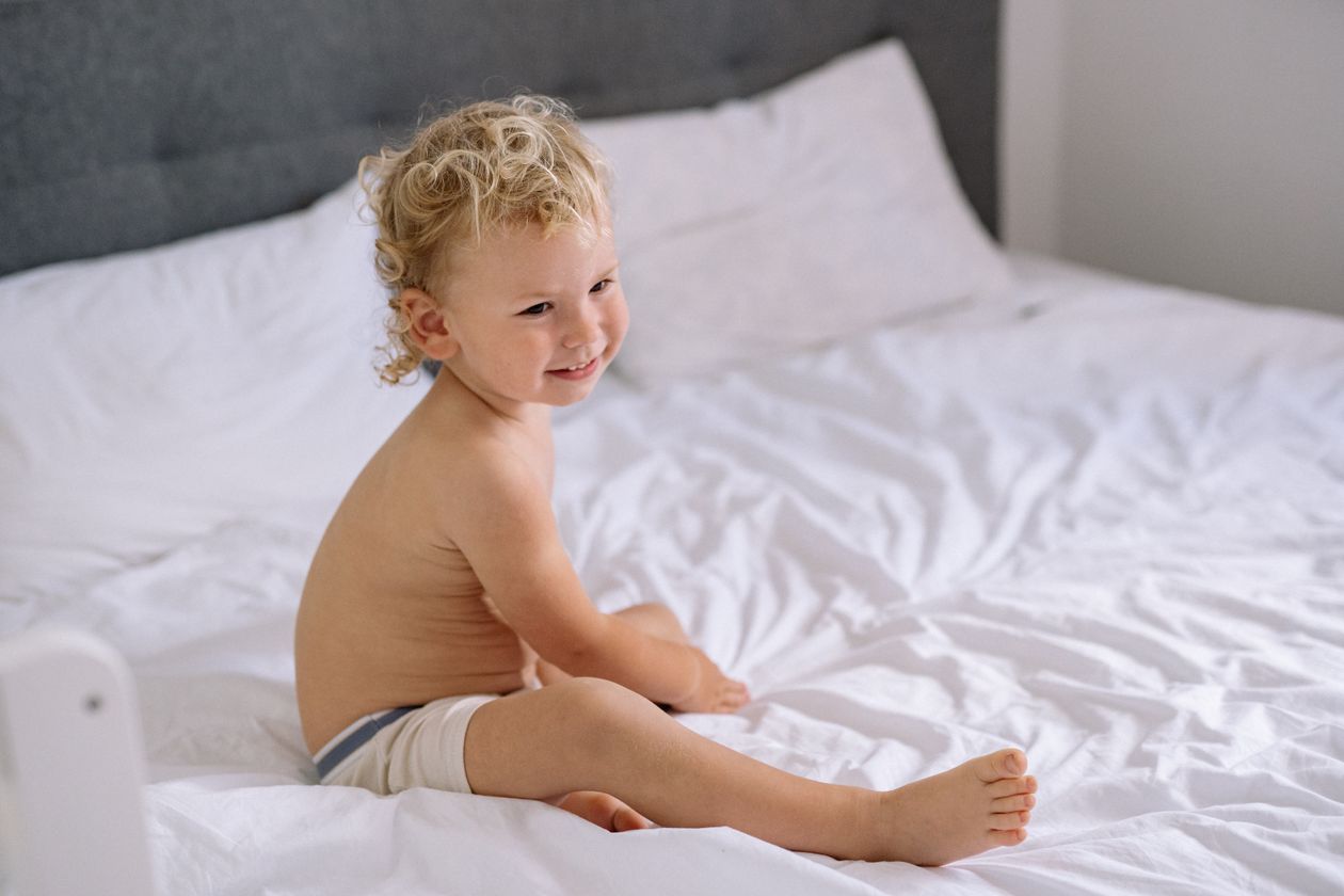 Smiling toddler sitting on a bed in a bright bedroom
